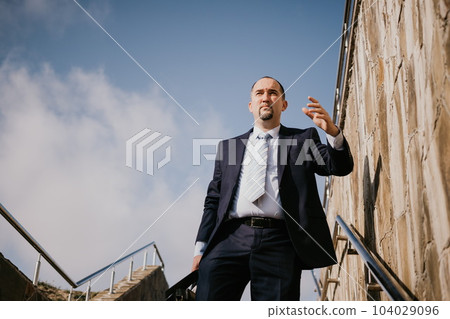 Confident middle age businessman with briefcase walking upstairs. Close-up of businessman wearing blue suit holding bag walking down the stairs Confident middle age businessman with briefcase walking upstairs. Close-up of businessman wearing blue suit holding bag walking down the stairs 104029096