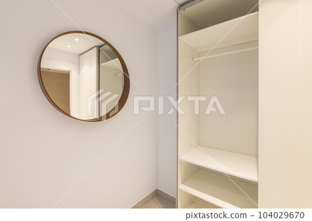 Close-up of a corner of a room with a mirror and an open empty wardrobe in light beige tones. The concept of a comfortable compact apartment after renovation 104029670