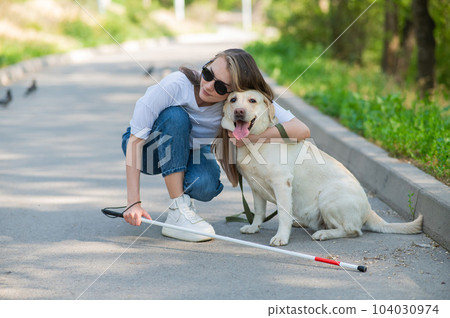 Blind young woman cuddling with guide dog on a walk outdoors. Blind young woman cuddling with guide dog on a walk outdoors. 104030974