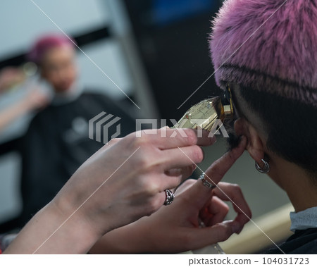 The hairdresser shaves the temple of a female client. Rear view of a woman with short pink hair in a barbershop. 104031723