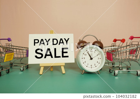 Pay Day Sale text message on paper card with wooden easel and trolley shopping cart 104032182