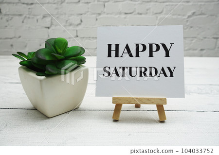 Happy Saturday text on wooden easel standing on white brick wall and wooden background Happy Saturday text on wooden easel standing on white brick wall and wooden background 104033752