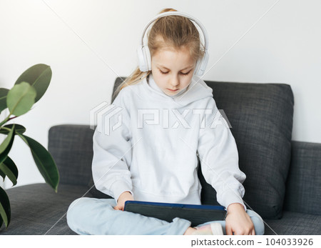 Little girl with headphones and tablet at home Little girl with headphones and tablet at home 104033926