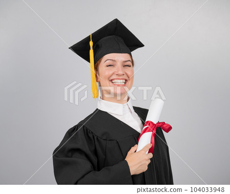 Smiling woman in graduation gown holding diploma on white background.  104033948