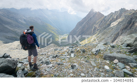 Fully packed mountaineer looking down into alpine valley , Austrian Alps, Europe Fully packed mountaineer looking down into alpine valley , Austrian Alps, Europe 104034891