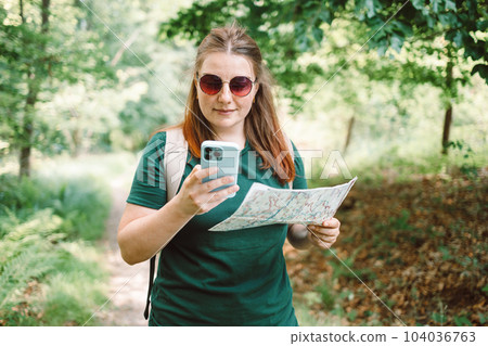 Young woman hiker reading map hiking trip looking to find place to go by phone 104036763