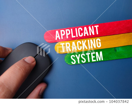 Wireless mouse and wooden stick with the word APPLICANT TRACKING SYSTEM on blue background 104037842