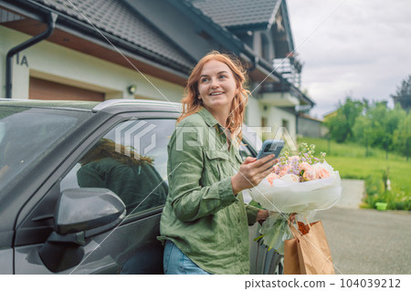 Female happy lady with bouquet of flowers and phone near car outdoors. Sexy carefree woman posing on the street background  104039212