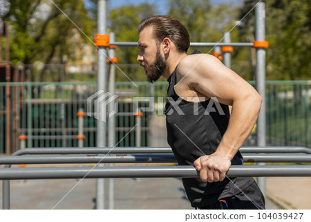 Athletic lebanese man in sportswear practicing dips on parallel bars, training triceps on playground 104039427