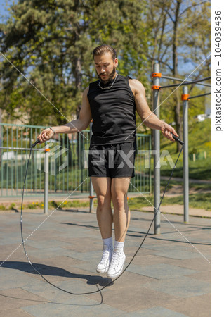 Athletic lebanese man in sportswear skipping rope doing jumping exercises on urban city playground Athletic lebanese man in sportswear skipping rope doing jumping exercises on urban city playground 104039436