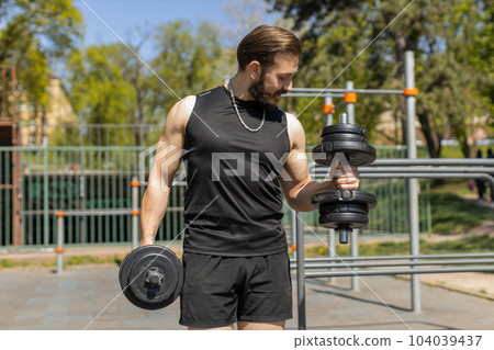 Athletic man doing arms weight lifting dumbbells exercises, pumping up arm bicep muscles outdoors Athletic man doing arms weight lifting dumbbells exercises, pumping up arm bicep muscles outdoors 104039437