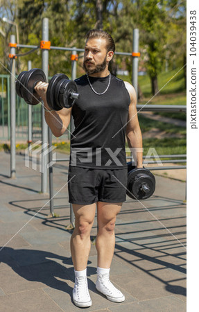 Athletic man doing arms weight lifting dumbbells exercises, pumping up arm bicep muscles outdoors 104039438