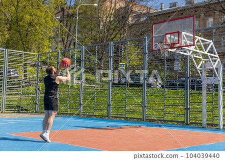 Athletic man in sportswear playing basketball game, successfully throws ball into the basket ring 104039440