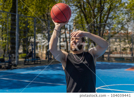 Athletic man in sportswear playing basketball game, successfully throws ball into the basket ring Athletic man in sportswear playing basketball game, successfully throws ball into the basket ring 104039441