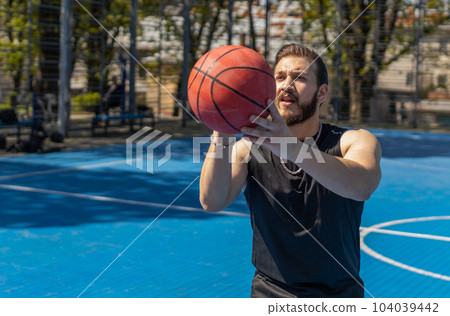 Athletic man in sportswear playing basketball game, successfully throws ball into the basket ring Athletic man in sportswear playing basketball game, successfully throws ball into the basket ring 104039442
