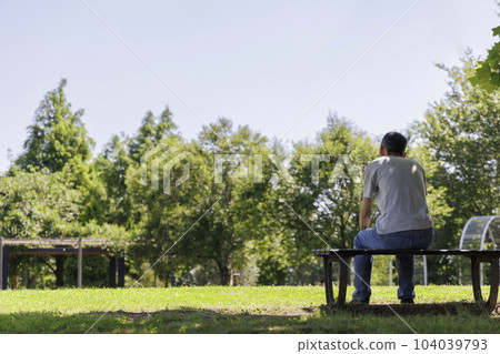 A middle-aged man sitting alone on a park bench 104039793