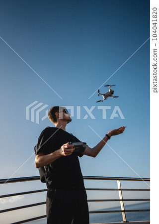 young photographer launching quadcopter drone from hand with remote controller 104041820