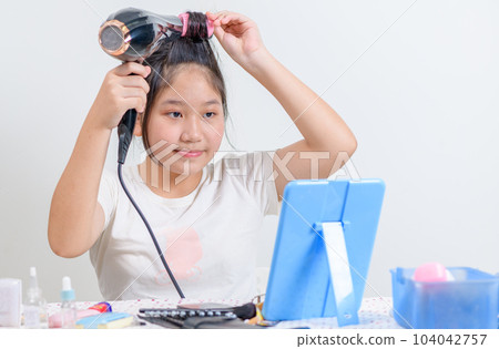 cute girl wearing hair rollers and holds a hair dryer and look at the mirror isolated on white 104042757