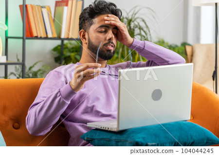 Tired indian man freelancer use laptop suffering from headache problem tension and migraine, stress 104044245