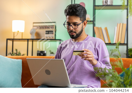 Young indian man using credit bank card and laptop, transferring money, purchases online shopping 104044254