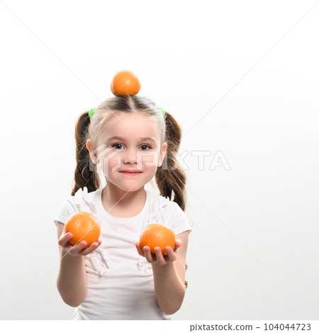 Portrait of a small beautiful girl on a white background with tangerines in her hands. 104044723