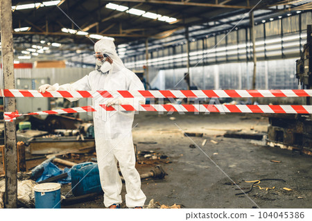 Worker in PPE safety suit with area closed barricade security tape in danger dirty area from virus infected chemical leak Worker in PPE safety suit with area closed barricade security tape in danger dirty area from virus infected chemical leak 104045386