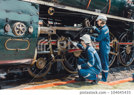 Train engineer team working service maintenance old dirty vintage classic steam engine locomotive in train repair workshop at train station. Train engineer team working service maintenance old dirty vintage classic steam engine locomotive in train repair workshop at train station. 104045435