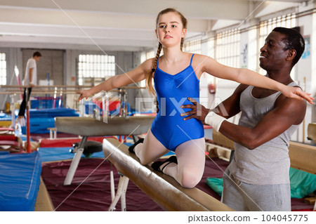 African male coach helping teenage girl doing gymnastic exercises on equipment African male coach helping teenage girl doing gymnastic exercises on equipment 104045775