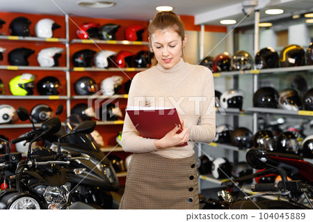 Positive young woman in moto salon choosing motorcycle to buy Positive young woman in moto salon choosing motorcycle to buy 104045889