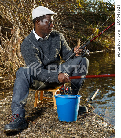Positive fisherman sitting near river Positive fisherman sitting near river 104045923