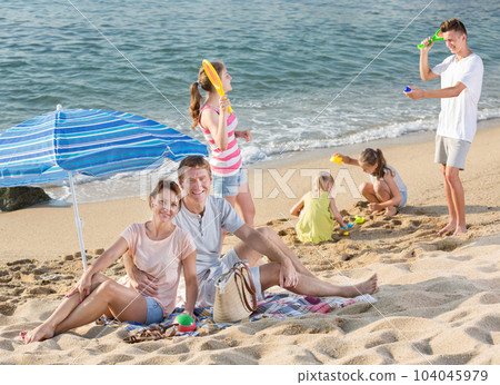 Parents and playing children on beach 104045979