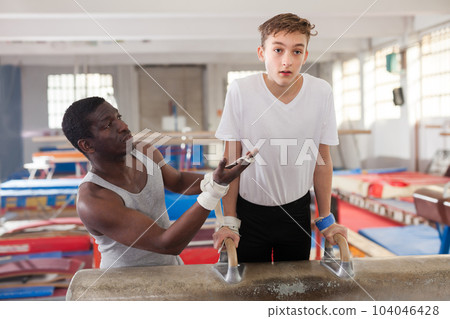 Attentive African male coach helping teenage boy 104046428