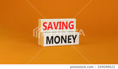 Saving money symbol. Concept words Saving money on wooden blocks on a beautiful orange table orange background. Business, support and saving money concept. Copy space. 104046622