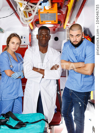 Three positive ambulance doctors posing in ambulance car with medical equipment 104046785