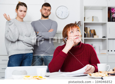 Distressed aged woman with paperwork and irritated family behind Distressed aged woman with paperwork and irritated family behind 104046852