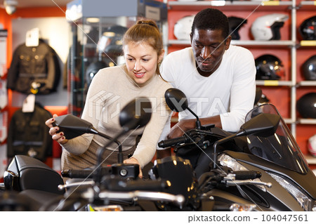 Portrait of satisfied man and woman looking new motorbike at motosalon showroom 104047561