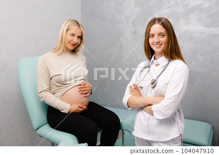 Gynecologist preparing for an examination procedure for a pregnant woman sitting on a gynecological chair in the office and smiling Gynecologist preparing for an examination procedure for a pregnant woman sitting on a gynecological chair in the office and smiling 104047910