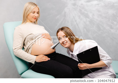 A gynecologist leans a stethoscope to a pregnant woman's belly and listens to the baby's heartbeat 104047912