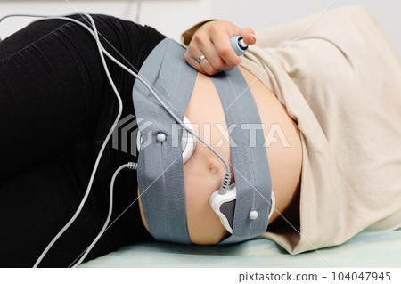 Woman pregnant checking fetal heart beat by fetal monitoring. Expectant mother with midwife adjusting sensors off cardiotocography Woman pregnant checking fetal heart beat by fetal monitoring. Expectant mother with midwife adjusting sensors off cardiotocography 104047945