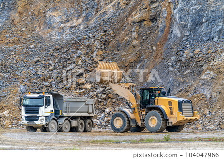 an excavator is loading a truck with stone at a quarry an excavator is loading a truck with stone at a quarry 104047966