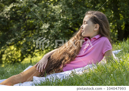 Little Adorable Asian Girl With Extra Long Hair Lying On Grass in Park. Brown Haired Child Having Fun, Enjoying Nature, Summertime. Carefree, Happy Childhood, Closeup, Horizontal Plane. 104047993
