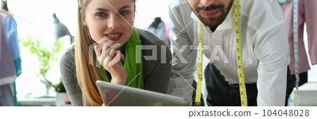 Man and woman designers are discussing new collection of clothes on digital tablet in workshop 104048028
