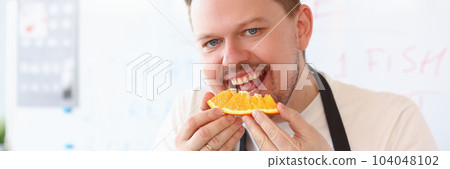 Red smiling male cook is biting orange 104048102