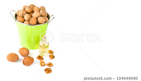 Walnut kernels, nuts in a bucket and bottled nut oil isolated on white . Free space for text. Wide photo. Walnut kernels, nuts in a bucket and bottled nut oil isolated on white . Free space for text. Wide photo. 104049090