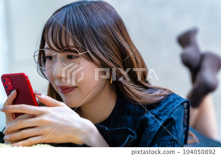 A woman with glasses lying down and using a smartphone A woman with glasses lying down and using a smartphone 104050892