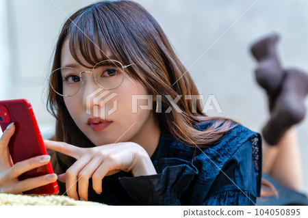 A woman with glasses lying down and using a smartphone A woman with glasses lying down and using a smartphone 104050895