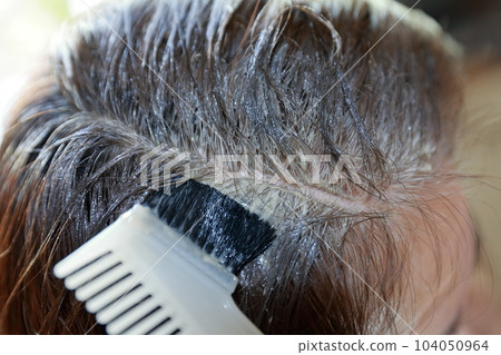 A woman dyeing her gray hair with a brush A woman dyeing her gray hair with a brush 104050964