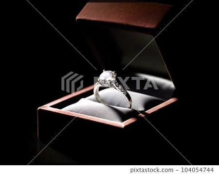 A realistic illustration of a sparkling diamond ring in a case on a black background A realistic illustration of a sparkling diamond ring in a case on a black background 104054744
