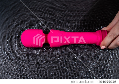 A woman holds a pink dildo in the water. Sex toy on a black background. 104055036