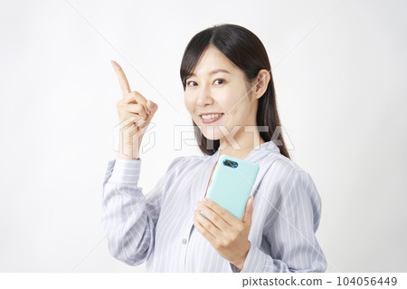 Middle-aged woman holding a smartphone and pointing to the left White background 104056449
